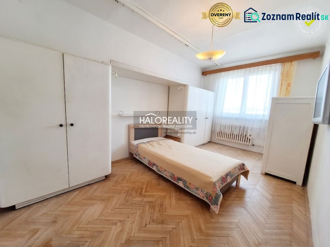 Hálószoba egy háromszobás lakásban, fa dekoros padlóval és egyszerű berendezéssel.