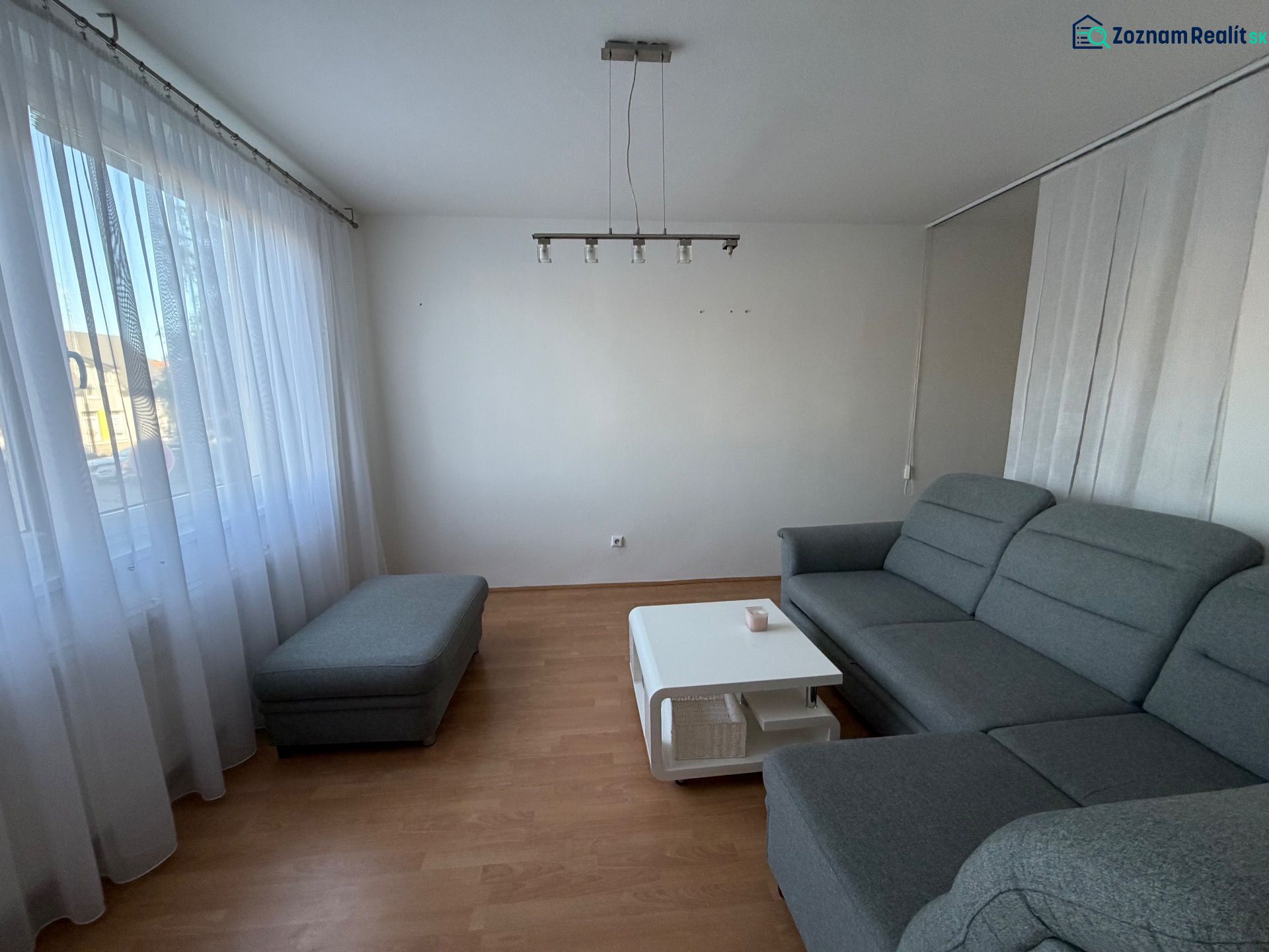 Nappali szürke kanapéval, asztallal és fa dekoros padlóval egy háromszobás lakásban.