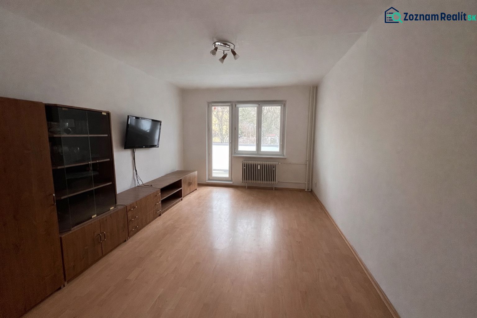 Nappali egy kétszobás lakásban, fa hatású padlóval és falra szerelt televízióval.