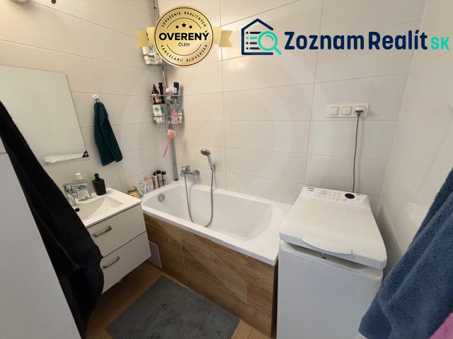 Fürdőszoba egy háromszobás lakásban káddal, mosdóval és mosógéppel, fehér csempékkel.