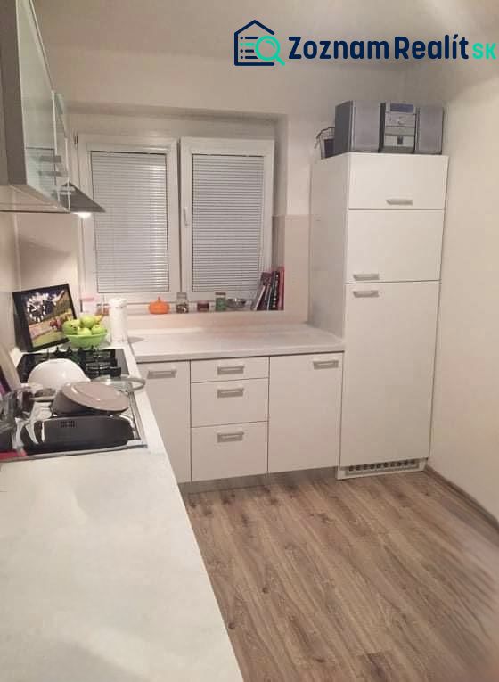 Konyha egy kétszobás lakásban fehér szekrényekkel és fa mintázatú padlóval.