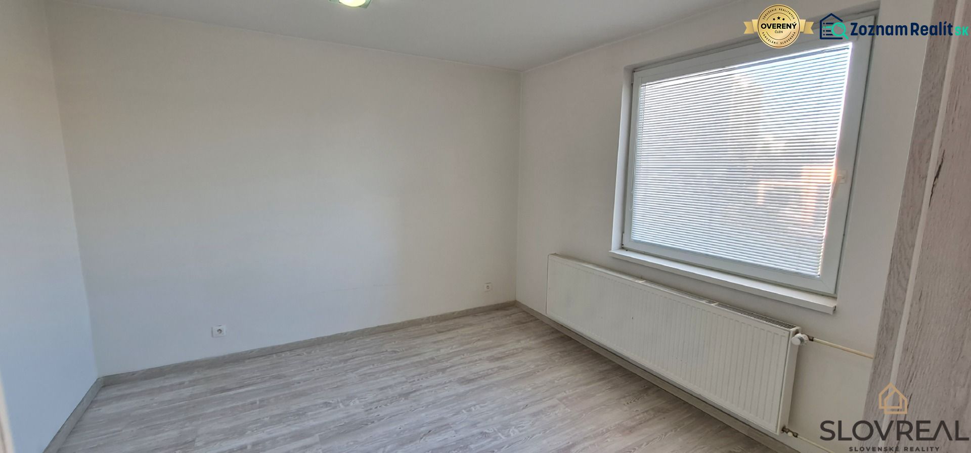 Szoba egy kétszobás lakásban fehér falakkal és fa dekorációjú padlóval.