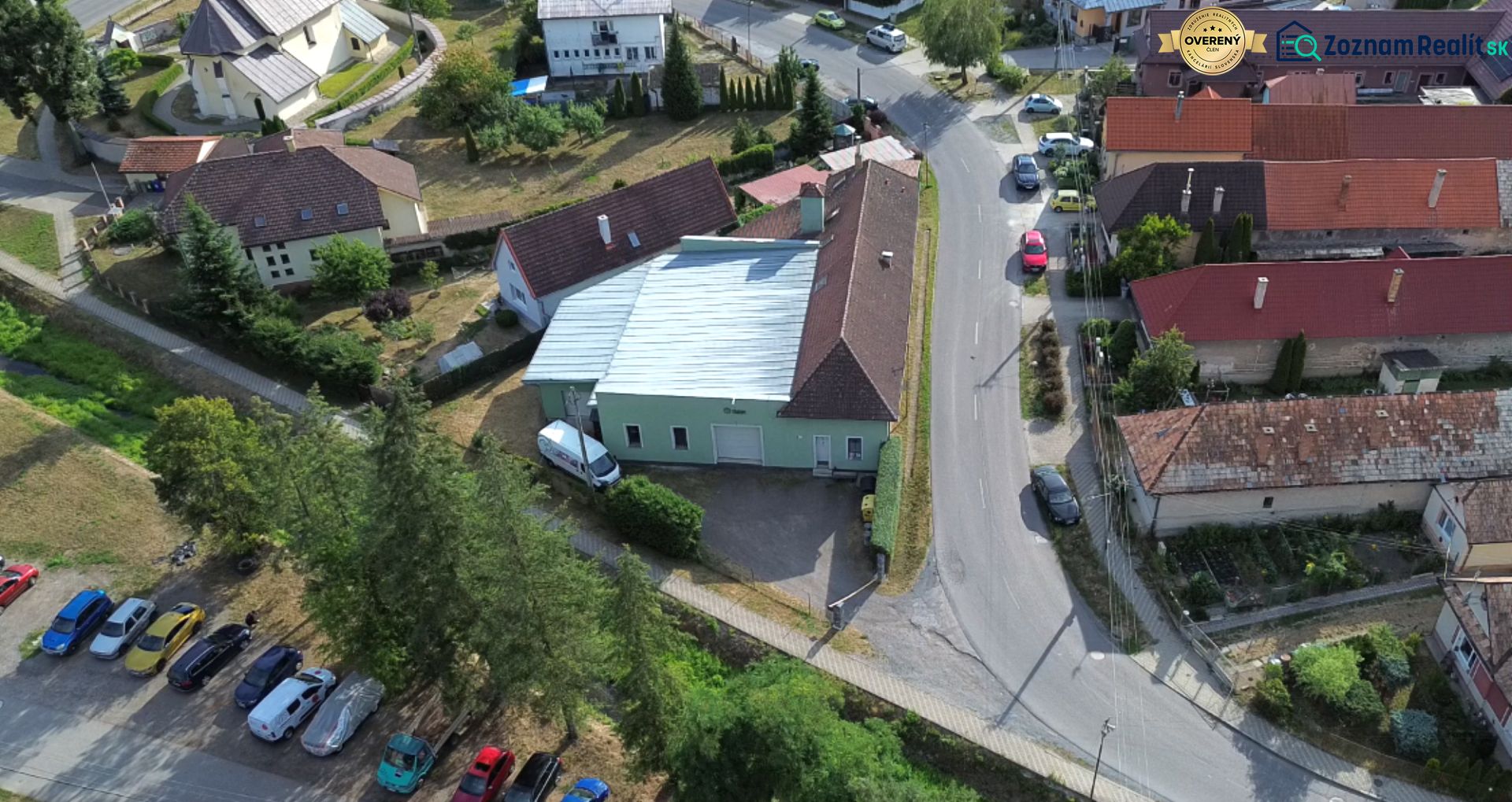 Légifelvétel a budčai gyártóüzemről, amelyet házak és zöldterületek vesznek körül.