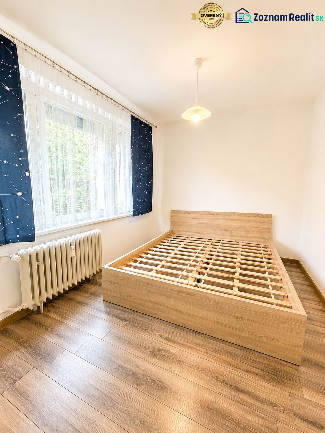 Hálószoba fa mintázatú padlóval és ággyal egy háromszobás lakásban.