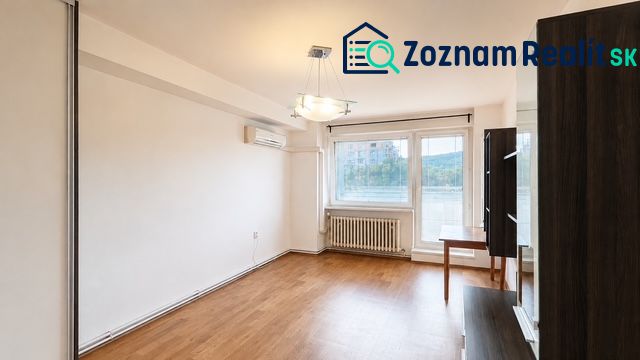 Nappali fa mintázatú padlóval, légkondicionálóval és nagy ablakkal egy háromszobás lakásban.