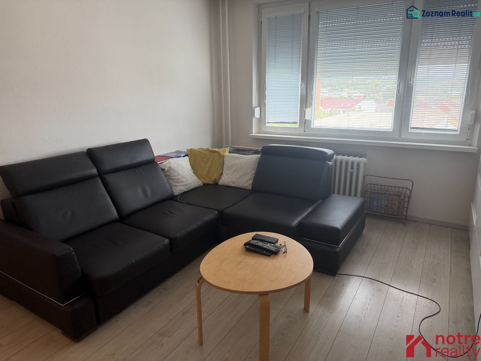 Nappali egy kétszobás lakásban fekete kanapéval és fa dekoros padlóval.