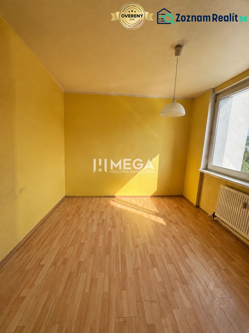 Sárga szoba nagy ablakkal és fa dekoros padlóval egy háromszobás lakásban.