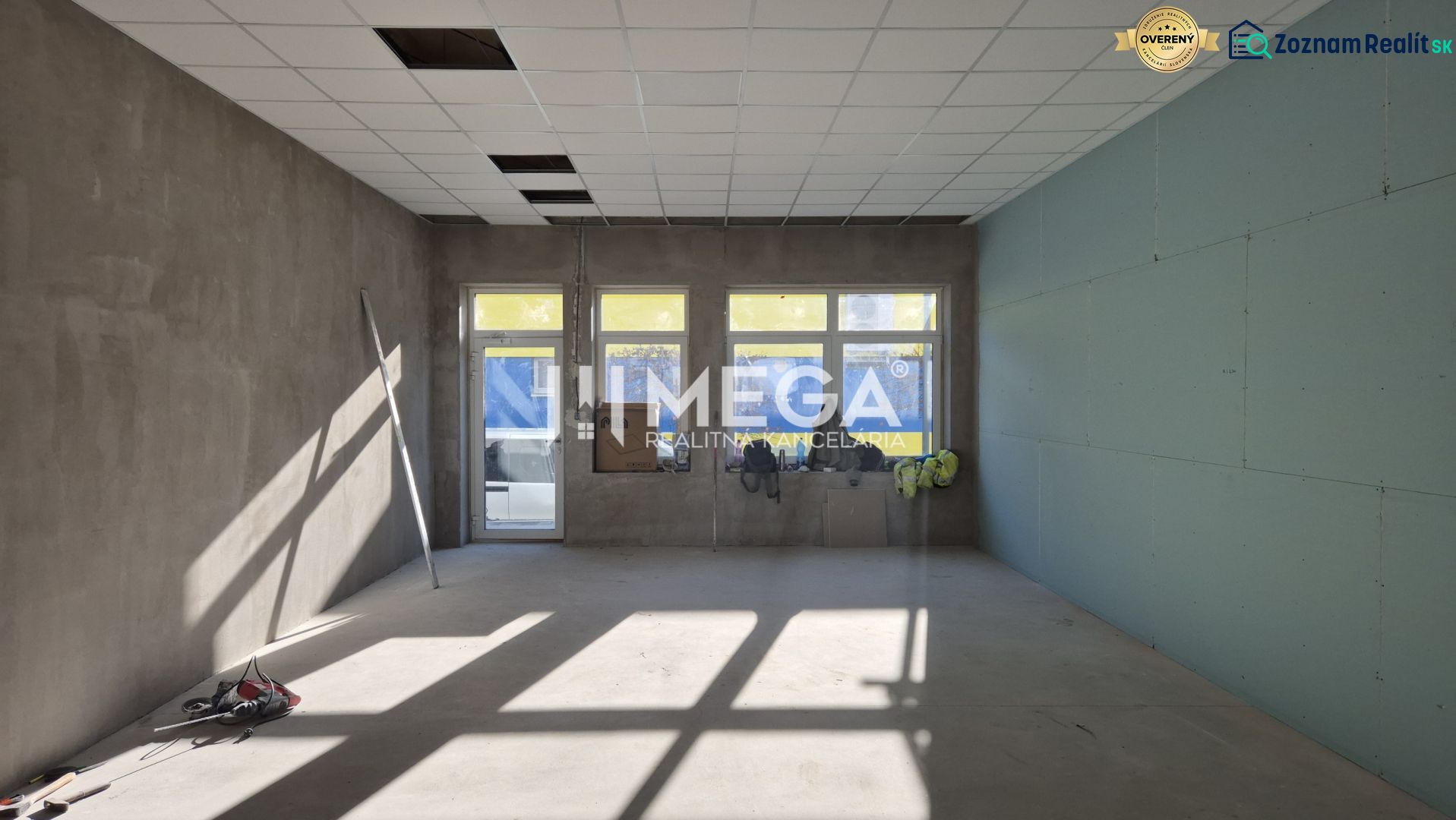Kereskedelmi helyiségek magas ablakokkal, betonpadlóval és fehér mennyezettel.