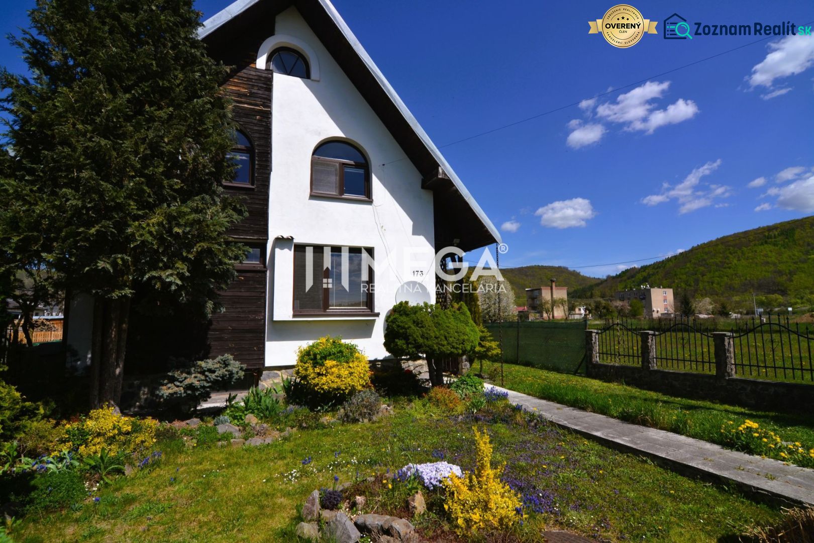 Családi ház Koskovce-ban rendezett kerttel és dombos háttérrel a kék ég alatt.