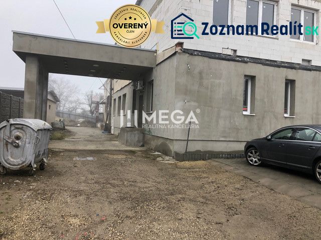 Épület az SNP utcában, Szinna, parkoló autóval és konténerrel kavicsos felületen.