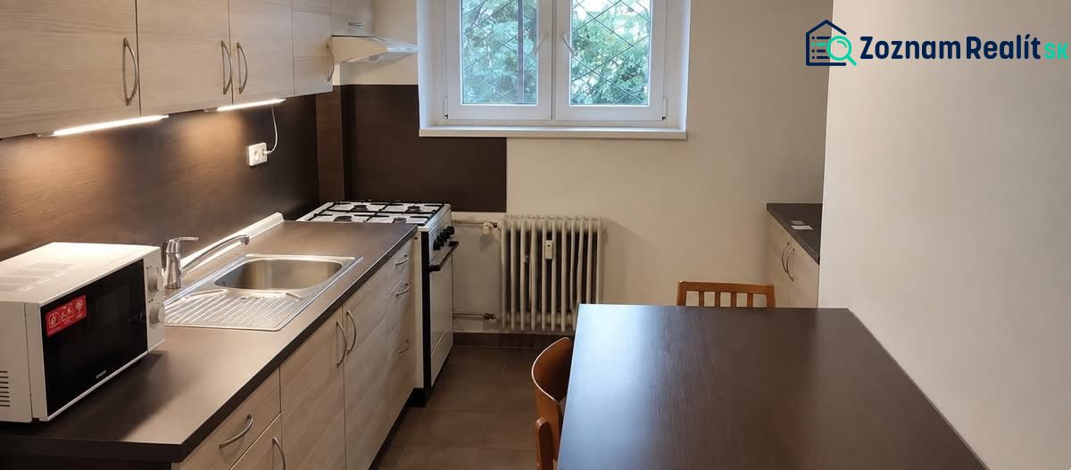 Konyha egy egyszobás lakásban gáztűzhellyel és mikrohullámú sütővel a sötét munkalapon.