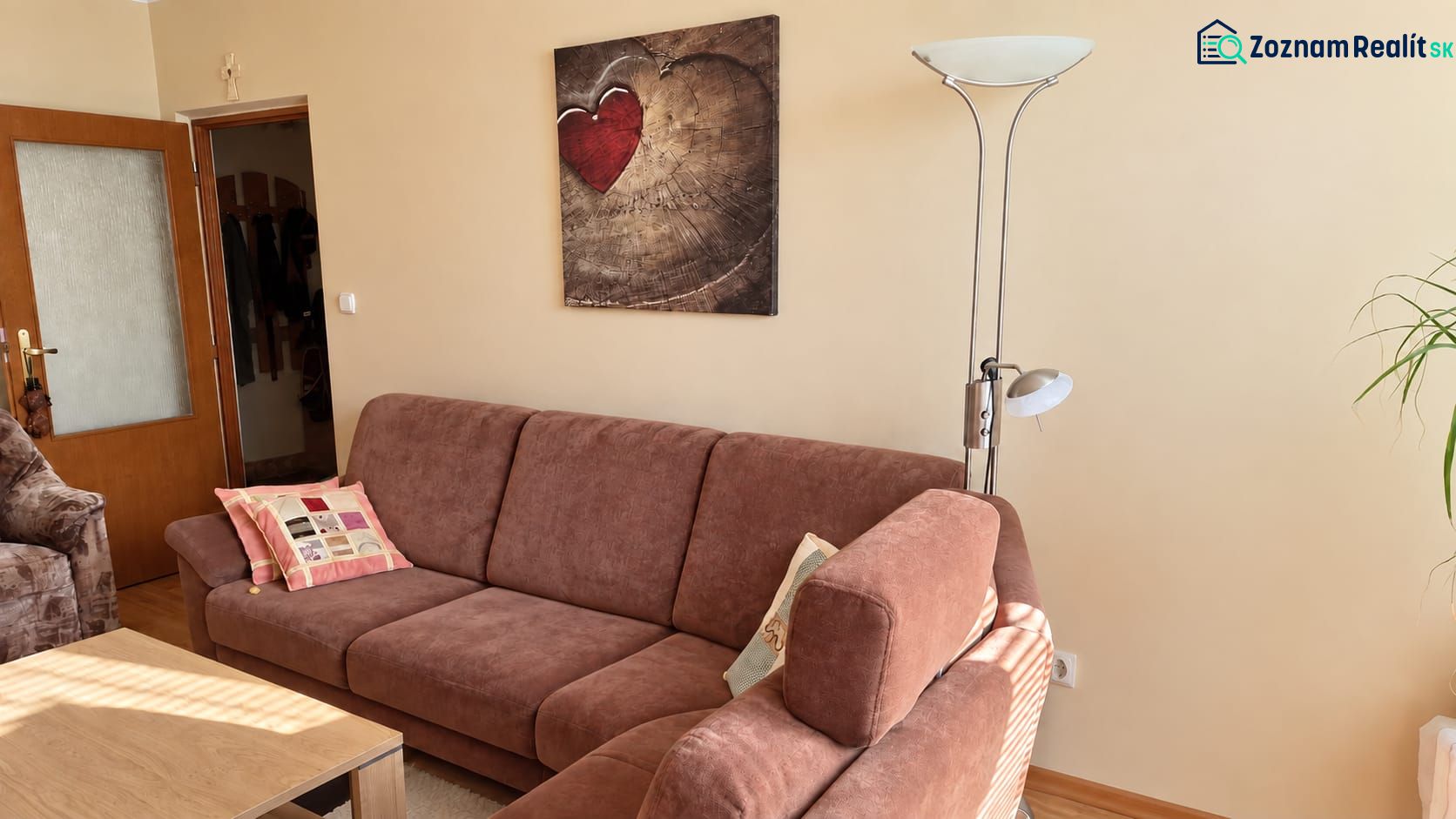 Kényelmes nappali kanapéval, lámpával és művészeti képpel egy háromszobás lakásban.