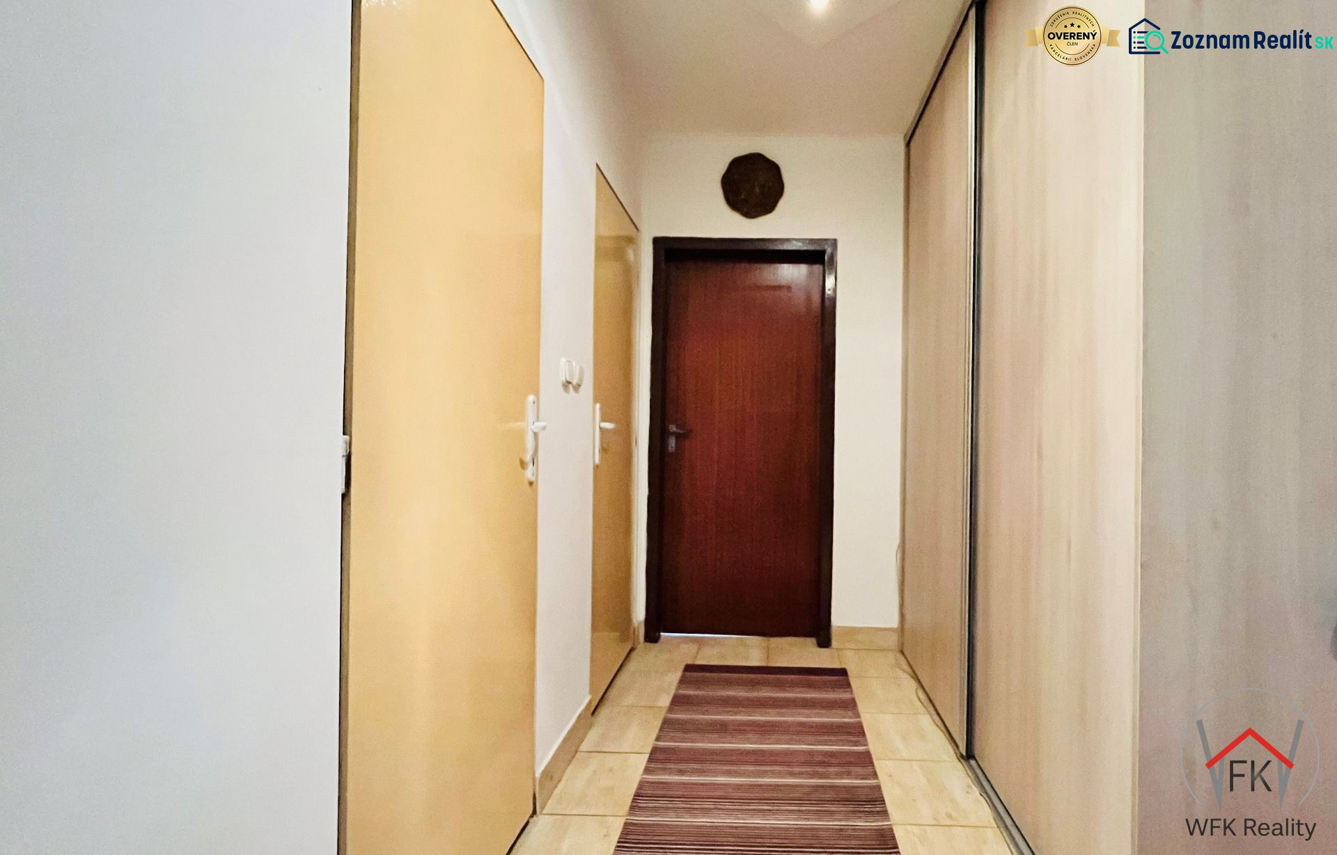 Folyosó egy 3 szobás lakásban tárolóhelyekkel és meleg tónusú szőnyeggel.