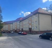 Bytový dom na ulici s parkovaním, možnosť 2-izbového bytu. Viditeľná križovatka v pozadí.