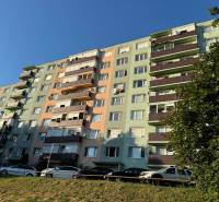 Obrázok ukazuje farebný bytový dom s balkónmi a odstavenými autami na ulici Boženy Němcovej.