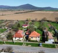 Rodinný dom v dedine obklopený poliami, kopcami a záhradami v panoramatickom prostredí.