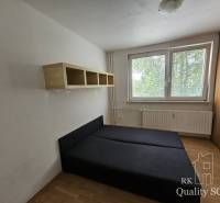 Hálószoba ággyal és polccal egy kétszobás lakásban. Ablakok kilátással a zöldre.