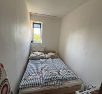Kis hálószoba ággyal egy háromszobás lakásban, egyszerű berendezés és fehér belső tér.
