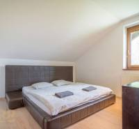 Hálószoba a nyaraló apartmanban kétágyas szobával, ablakkal, fa bútorokkal és tetőlejtésekkel.