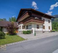 Nyaraló apartman a Magas-Tátrában, zölddel körülvéve, kék égbolt, hegyek a háttérben.