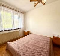 Hálószoba ággyal, ablakkal és fa padlóval egy családi házban.