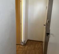 Egy szobás lakás folyosója fa padlóval, fehér falakkal és nyitott ajtókkal.