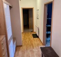 Folyosó egy kétszobás lakásban világos fa bútorokkal és nyitott ajtókkal.