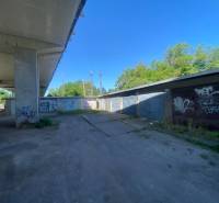 Garázsok Zólyomban a híd alatt, graffitikkel a falakon és parkoló autóval.