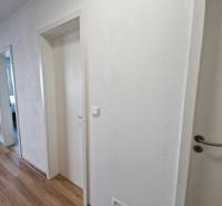 Folyosó egy 2 szobás lakásban, fehér ajtók és fa padló, modern bútorok a háttérben.