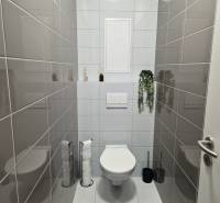 Fürdőszoba WC-vel egy kétszobás lakásban, sötétszürke csempékkel a falakon.
