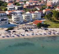 Strand napozóágyakkal és napernyőkkel, mögötte házak és épületek az üdülőhelyen.
