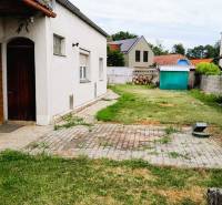 Egy családi ház udvara Potzneusiedlben, gyep, kerti házikó és templomtorony a háttérben.