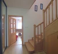 Családi ház belső tere fa lépcsővel, nappaliba vezető bejárattal és tárolóhellyel.