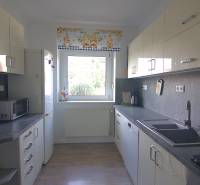 Családi ház konyhája fehér szekrényekkel, nagy ablakkal és háztartási gépekkel.