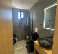 A nyaraló apartman fürdőszobája zuhanyzóval, fekete mosdóval és megvilágított tükörrel.