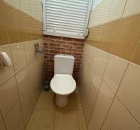 WC a háromszobás lakásban barna csempékkel és ablakkal.