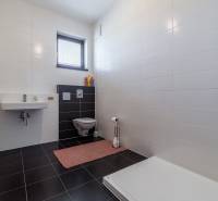 Fürdőszoba egy családi házban fehér csempékkel, mosdóval, WC-vel és zuhanyzóval.