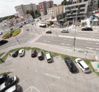 A Dunaszerdahelyi Fő utcán található körforgalom, körülötte lakóházak és parkoló található.