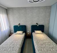 Kétszemélyes hálószoba geometrikus tapétával és modern világítással egy üdülő apartmanban.