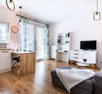 Nappali egy kétszobás lakásban kanapéval, TV-vel, étkezőasztallal és modern lámpákkal.
