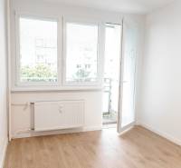 A 2 szobás lakásban van egy világos szoba erkélyajtóval és fa padlóval.
