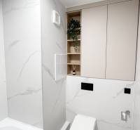 Minimalista fürdőszoba egy kétszobás lakásban WC-vel, káddal és tárolóhelyekkel.