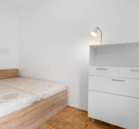 Hálószoba ággyal és komóddal egy kétszobás lakásban, fa mintázatú padlóval.