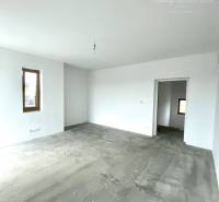 Tágas szoba egy családi házban betonpadlóval és fehér falakkal.