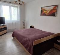 Hálószoba egy háromszobás lakásban ággyal, televízióval és faldekorációval.