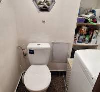 Fürdőszoba egy háromszobás lakásban WC-vel, mosógéppel és tisztítószerekkel teli polcokkal.