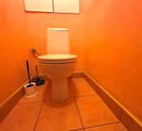 Narancssárga WC egy háromszobás lakásban, a WC-kefe a helyiség sarkában.