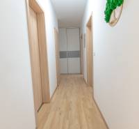 Világos folyosó fa padlóval és néhány fehér ajtóval egy háromszobás lakásban.