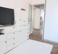 Fehér nappali egy 4 szobás lakásban, TV-vel, szekrényekkel és fa padlóval.