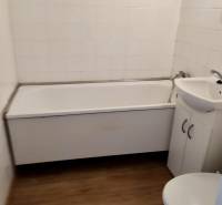 Fürdőszoba egy egyszobás lakásban káddal, mosdóval és WC-vel, fa hatású csempével.